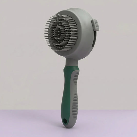 Brosse de toilettage ronde pour chien et chat, manche ergonomique vert et gris antidérapant, picots métalliques fins rétractables pour un nettoyage facile, vue de face sur fond neutre.