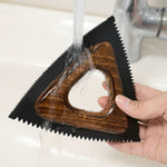 Main rinçant la brosse anti-poils triangulaire sous l'eau d'un robinet pour montrer la facilité de nettoyage du silicone, fond de salle de bain.
