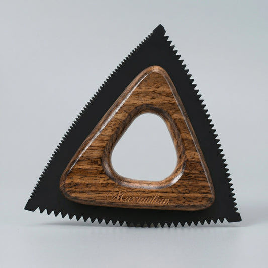 Outil de retrait de poils d'animaux triangulaire avec bords crantés en silicone noir et centre ergonomique en bois naturel, posé sur fond gris neutre.