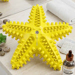 Jouet de soin dentaire pour chien en forme d'étoile de mer jaune vif avec ventouse, posé sur un rebord de salle de bain à côté d'accessoires de toilettage.