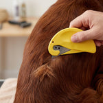 Main utilisant une brosse de précision jaune pour couper et démêler en toute sécurité un nœud dans le pelage long et roux d'un chien.